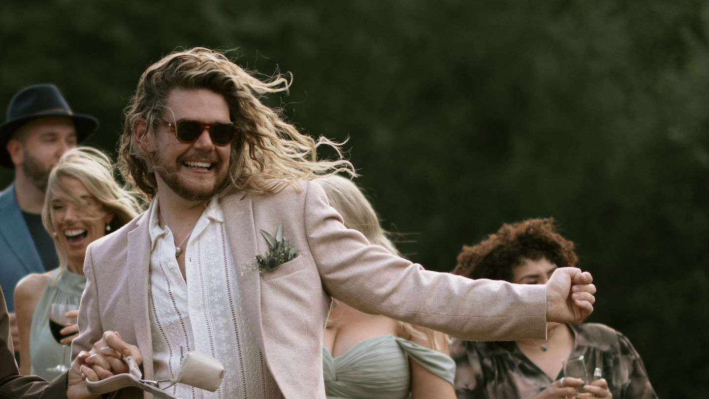 Man in a light suit and sunglasses dancing with a woman in a green dress at an outdoor event.